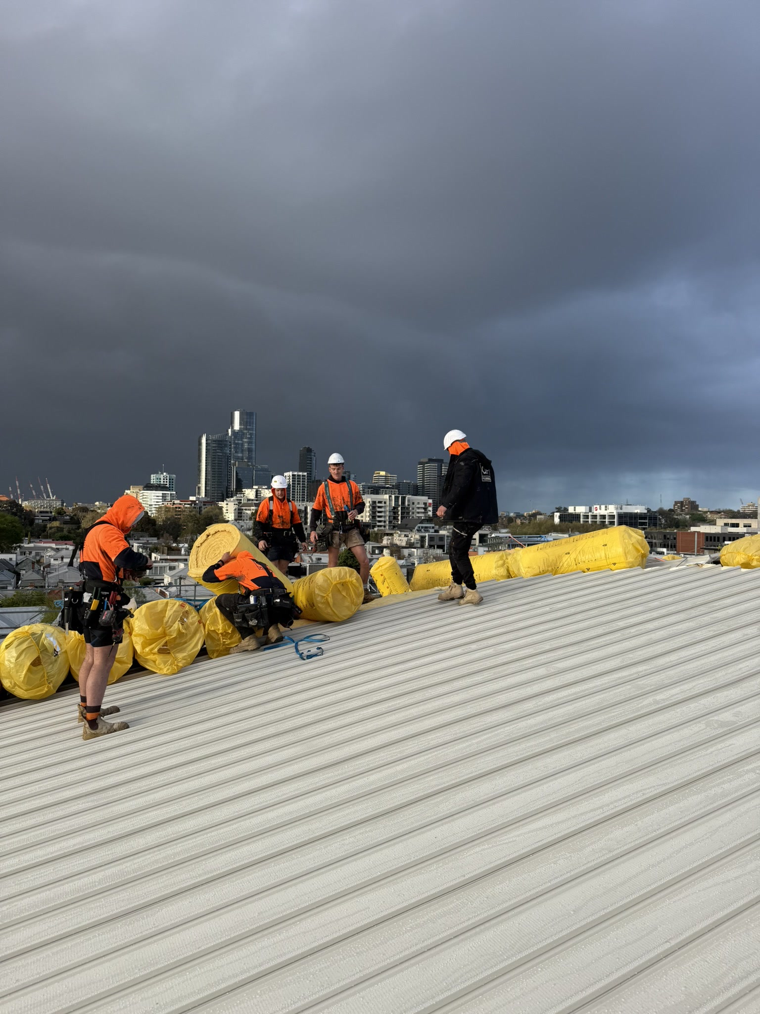 QP crew laying insulation on the Richmond Primary School roof with the Melbourne skyline behind